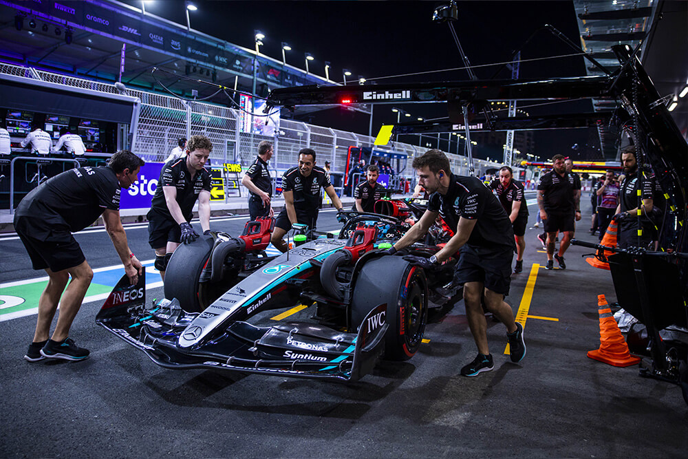 Mehrere Mechaniker des Mercedes-AMG PETRONAS F1 Teams mit einem Formel-1-Wagen in der Boxengasse bei Nacht.