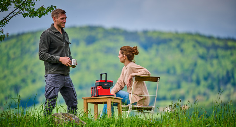 ein Mann und eine Frau sitzen im Garten und trinken Kaffee aus der Einhell Akku-Kaffeemaschine