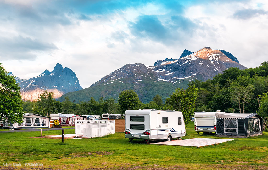 Ein Campingplatz mit Wohnwagen und Wohnmobilen vor einer Kulisse beeindruckender, schneebedeckter Berge und üppiger grüner Vegetation.