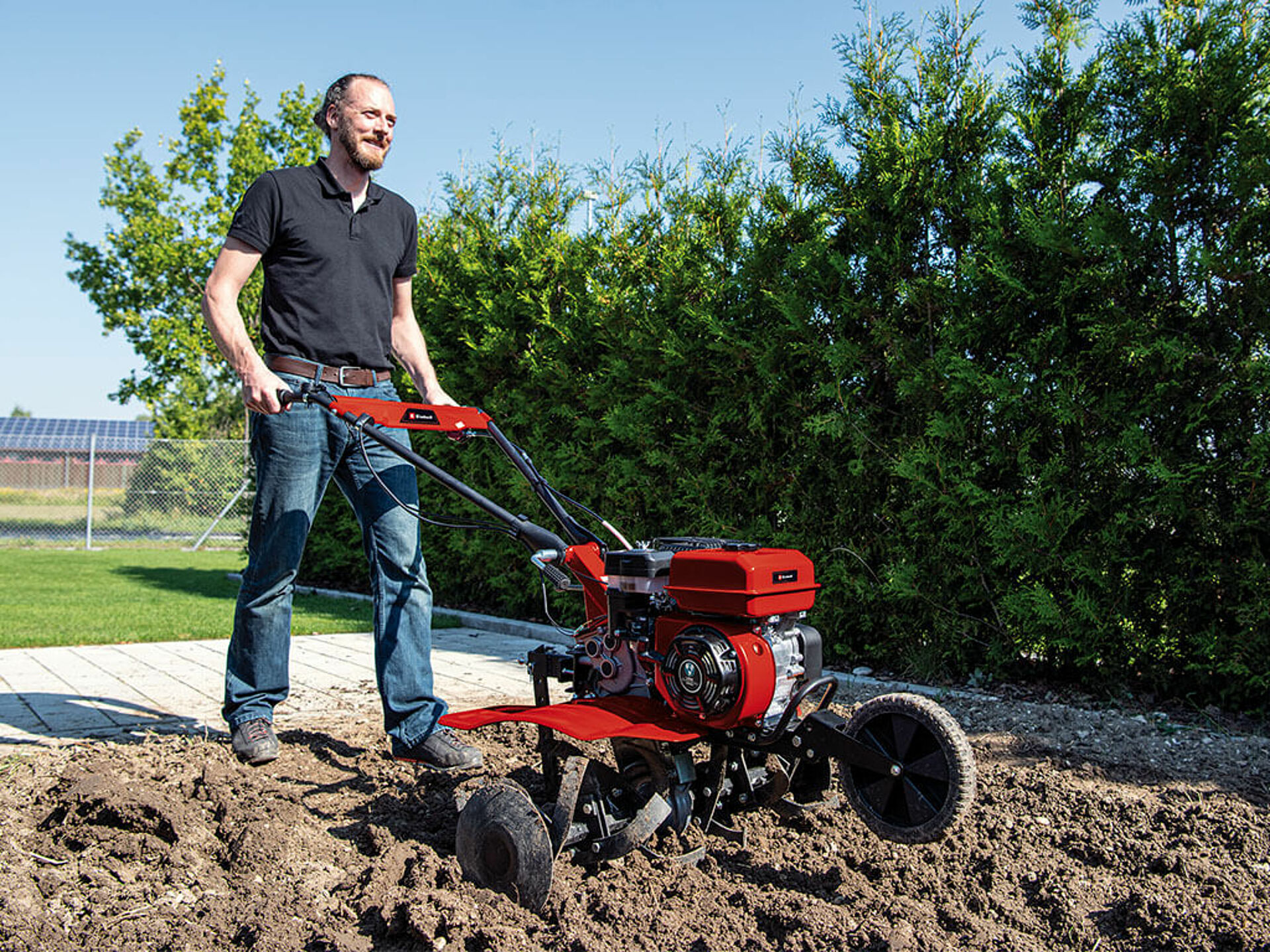 Ein Mann bearbeitet den Erdboden im Garten mit einer Benzin-Motorhacke von Einhell.