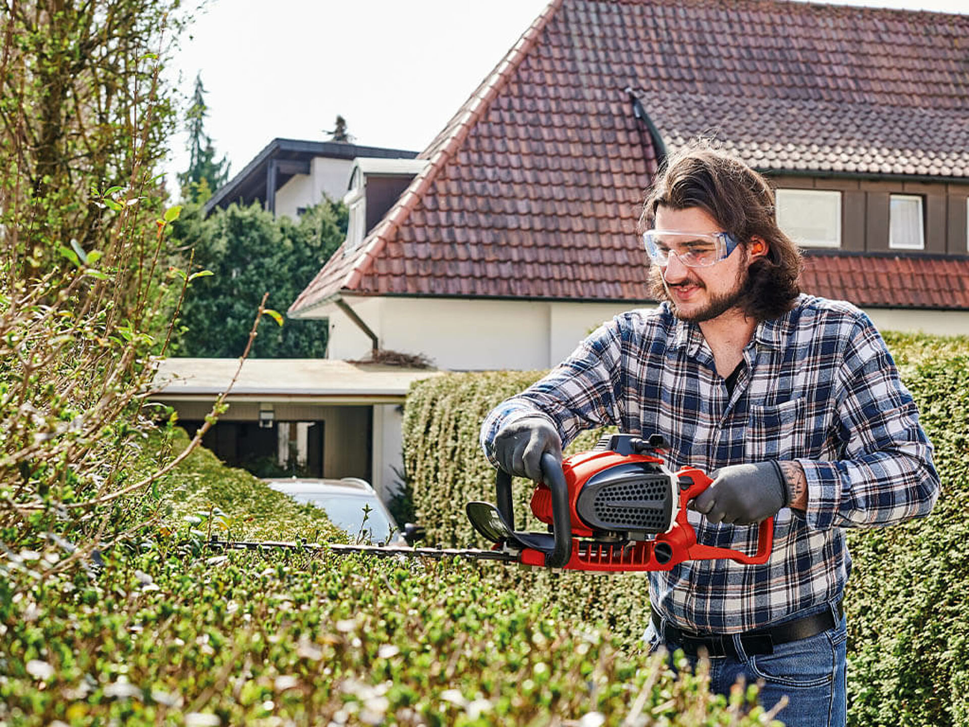 Ein Mann schneidet eine Hecke mit einer kraftvollen Benzin-Heckenschere von Einhell.