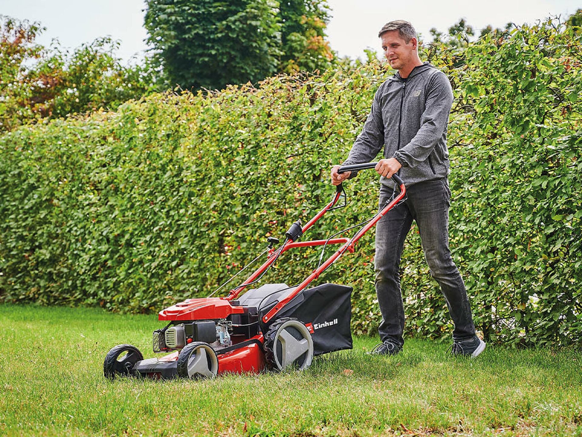 A man cuts the grass in his garden with a powerful Einhell petrol lawnmower.