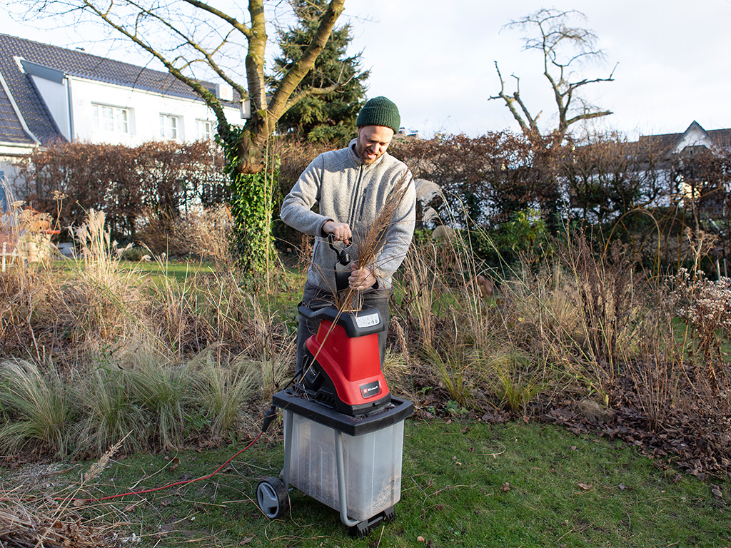 Ein Mann benutzt einen Gartenhäcksler um Äste zu zerkleinern.