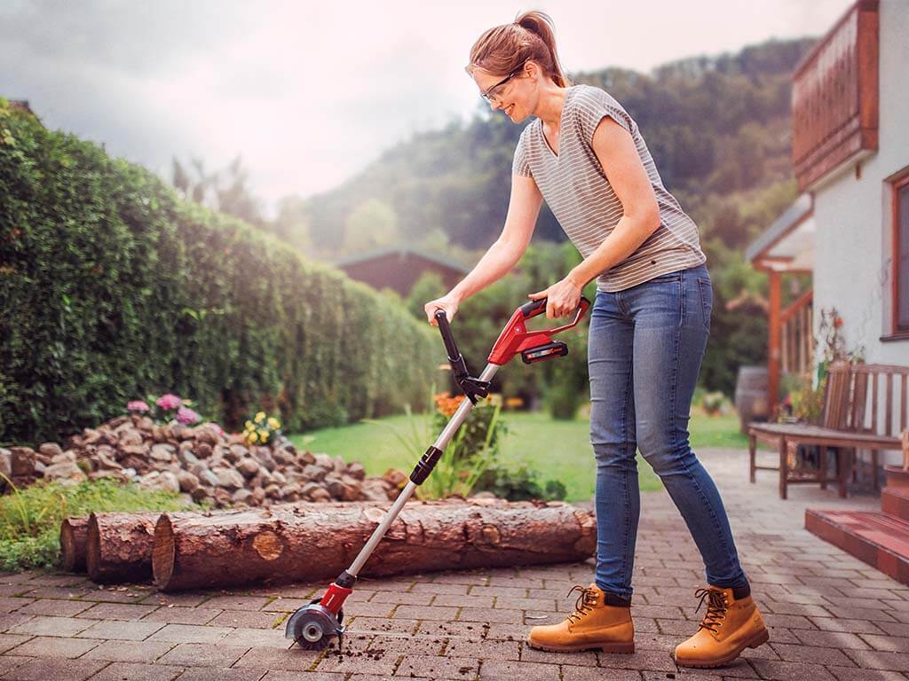 A woman cleans the spaces between paving stones with an Einhell joint cleaner