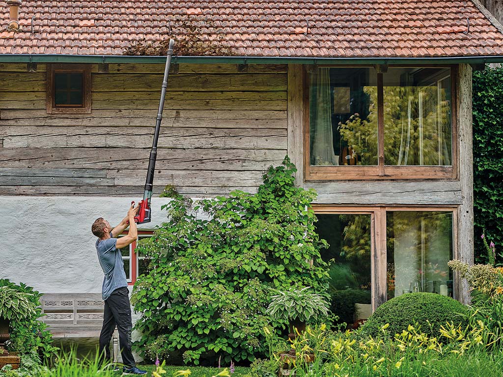 A man cleans a gutter with an Einhell cordless leaf blower and an extension.