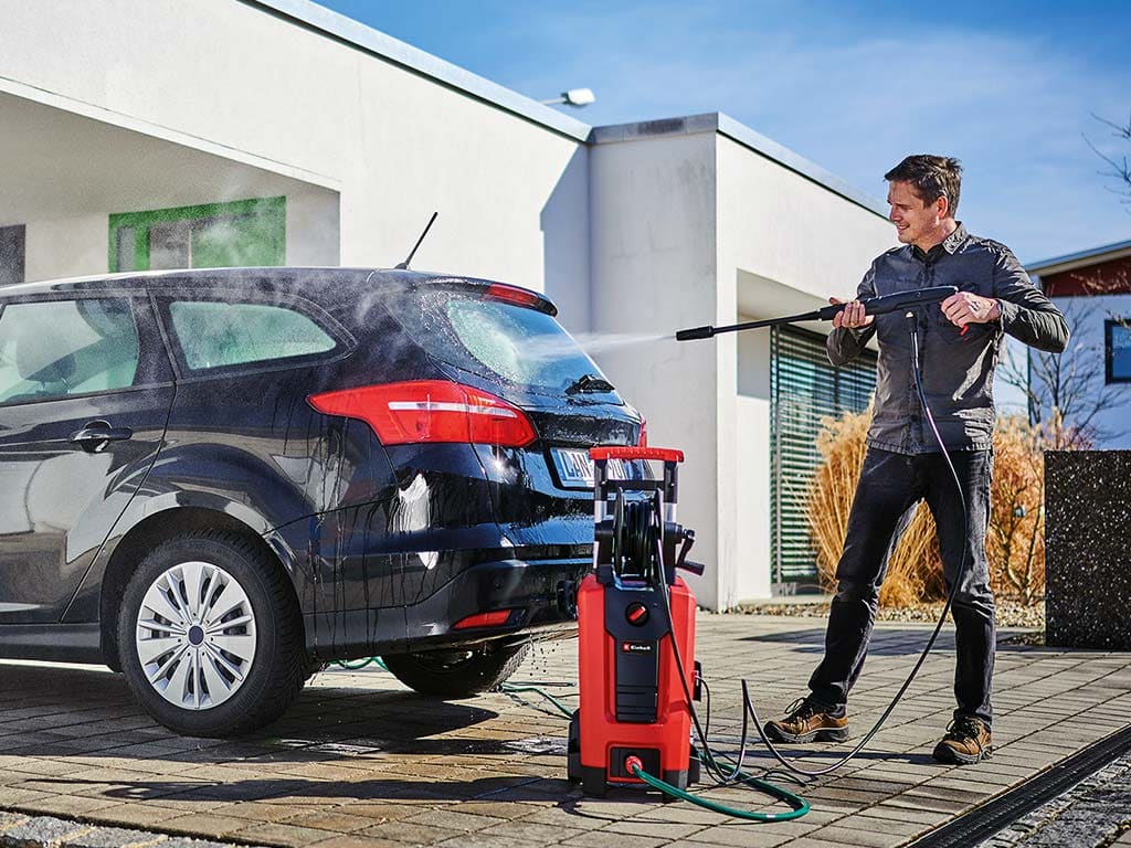 A man cleans his car with a pressure washer.