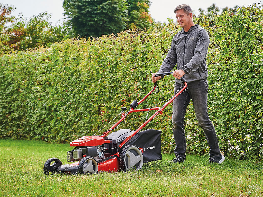 Ein Mann mäht den Rasen in seinem Garten mit einem kraftvollen Benzin-Rasenmäher von Einhell.