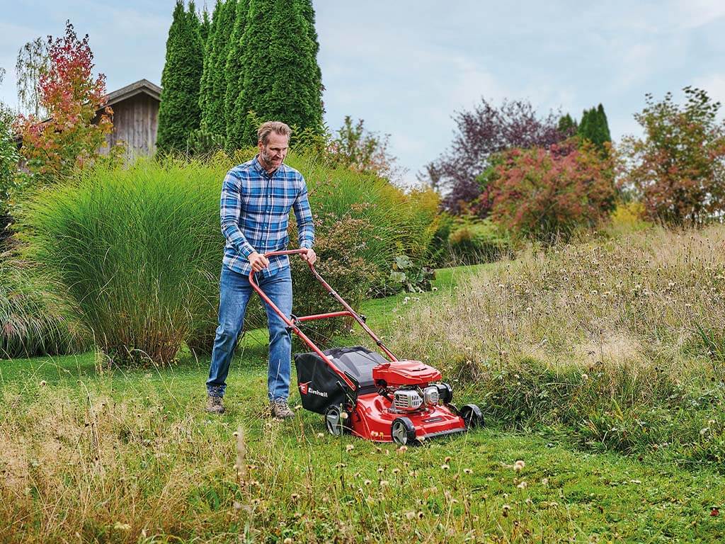 A man cuts tall grass with a petrol lawnmower from Einhell.