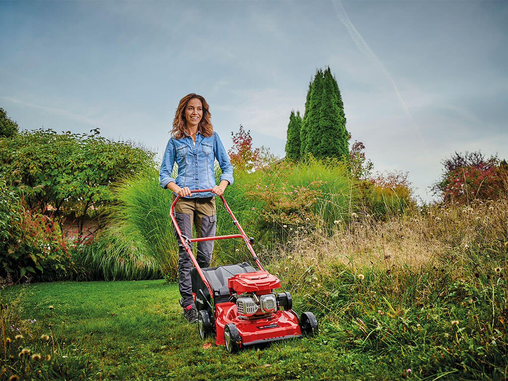 Eine Frau mäht hohes Gras mit einem leistungsstarken Benzin-Rasenmäher von Einhell.