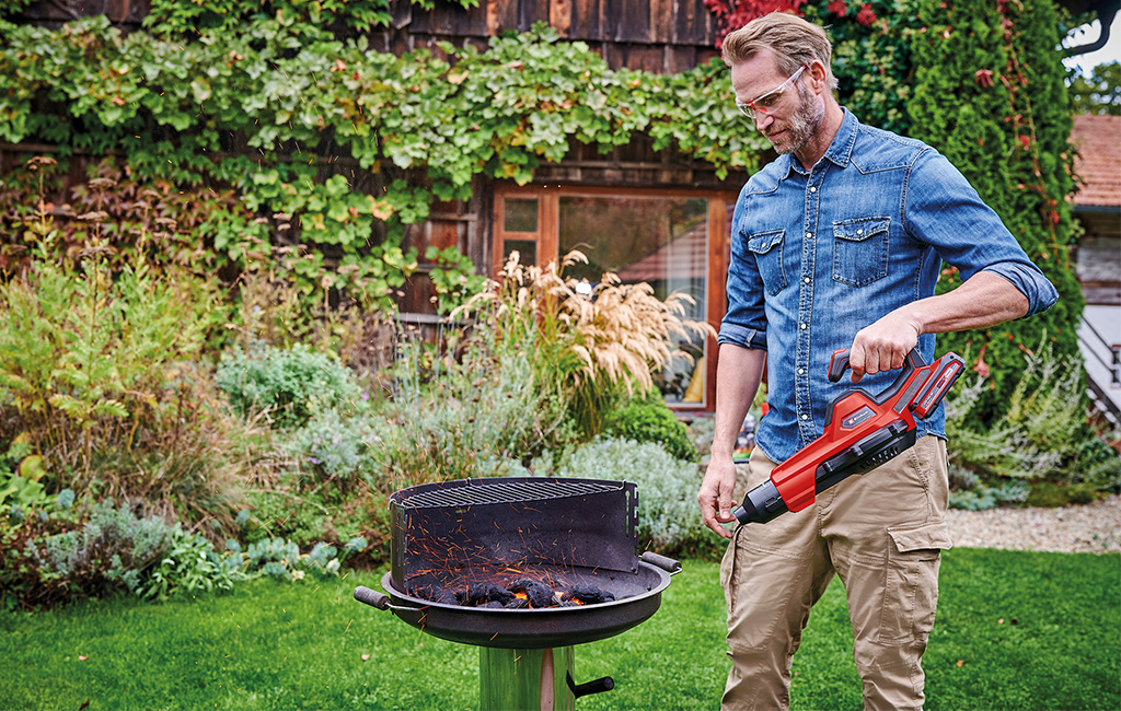 A man is using the einhell cordless blower to light the grill