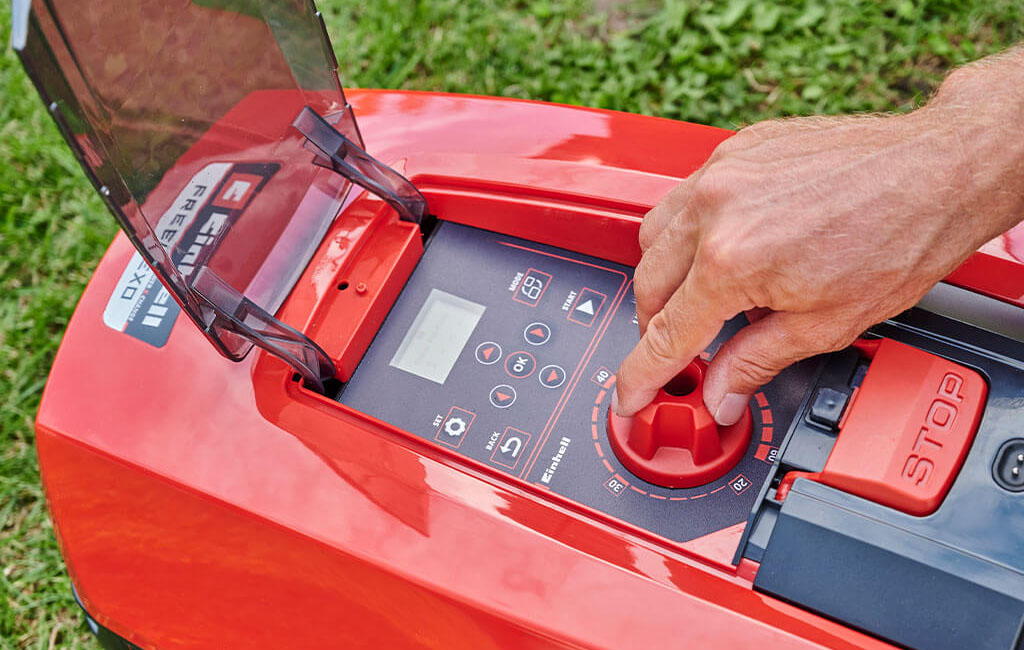 A male hand turns a knob on the robotic lawnmower to set the cutting height.