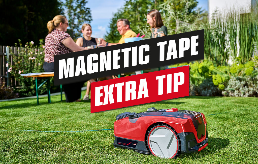 A robot lawnmower mowing lawn in a garden where four people are sitting at a table. The text in de picture says: Magnetic tape - Extra-Tip.