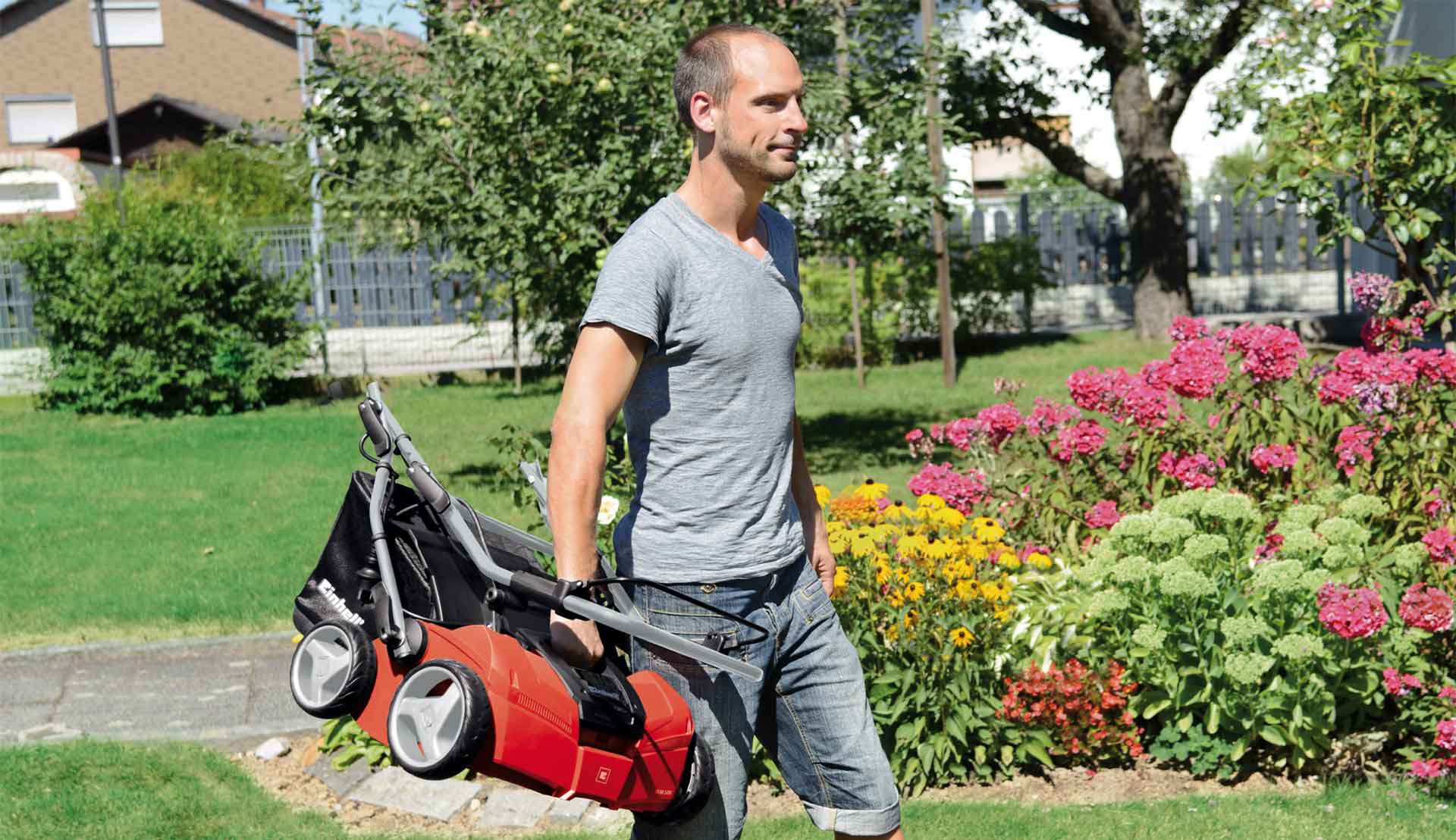 a man holding one of the Einhell scarifier and carrying around the garden