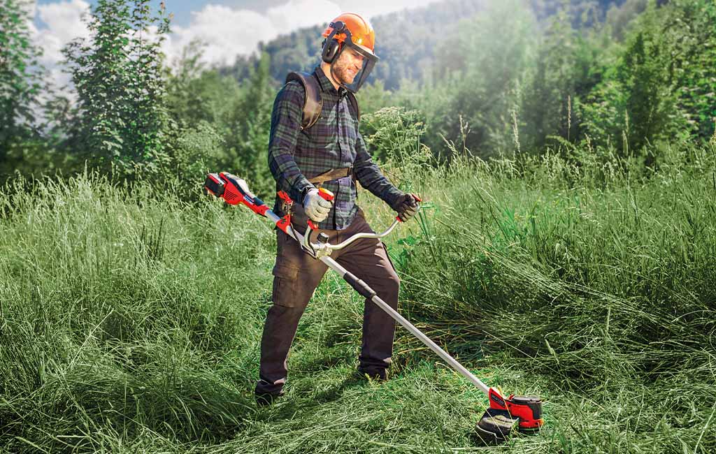 A man with a scythe mowing a meadow with high undergrowth.