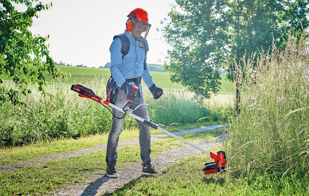 A man in protective clothing mowing a wayside with a cordless scythe.