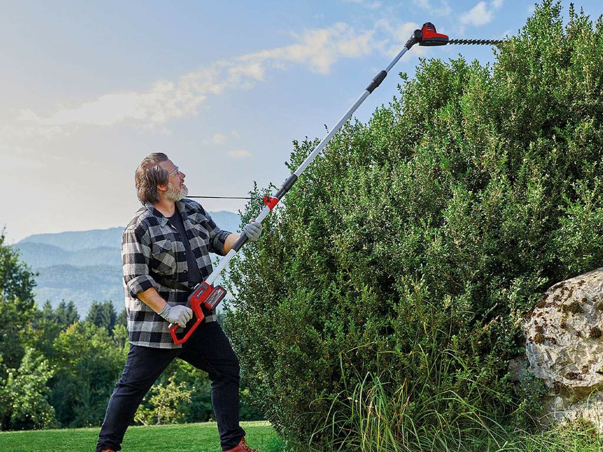 a man cuts his hedge with a retractable hedge trimmer