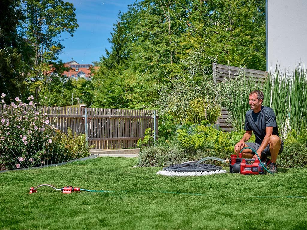 Ein Mann kniet im Garten neben einer Akku-Gartenpumpe.
