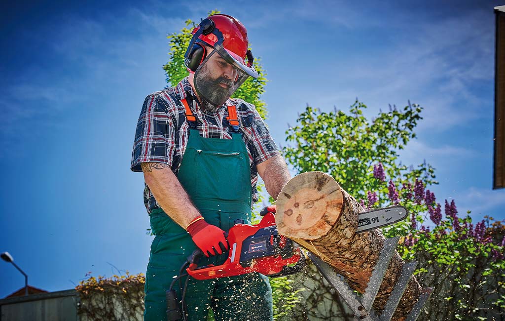 A man sawing a tree trunk into pieces with a chainsaw on a chainsaw stand.