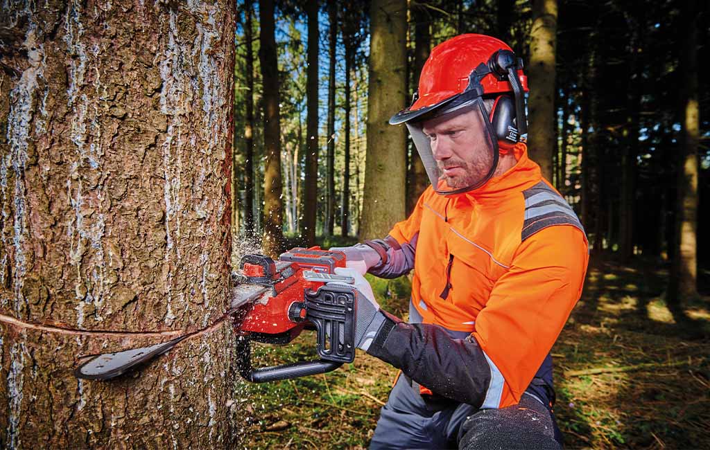 A man in the forest cutting down a tree with a chainsaw.