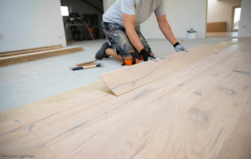 Nahaufnahme einer Person, die Holzdielen auf den Boden legt.