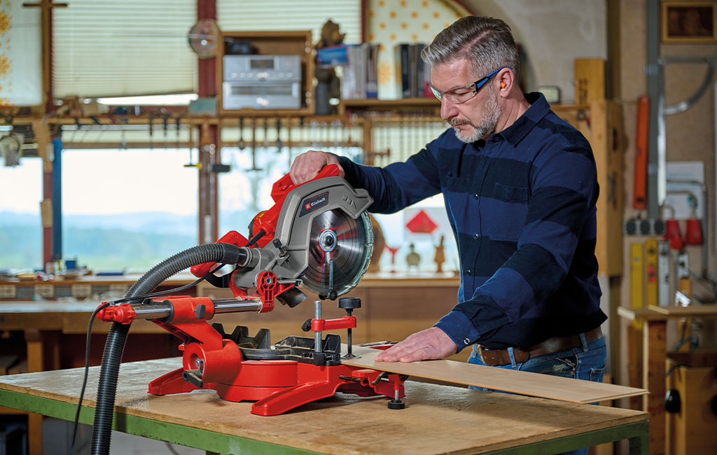 Ein Mann benutzt eine Einhell Kappsäge, um Holzdielen zu schneiden.