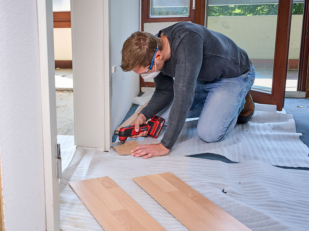 Ein Mann schneidet mit einem Einhell Akku-Multitool Laminatdielen in einem Raum während der Renovierung zu.