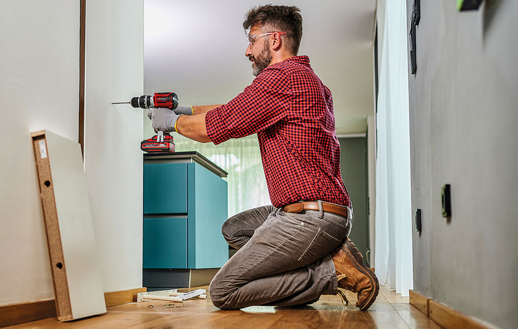 A man drills a hole in a wall using an Einhell cordless impact drill.