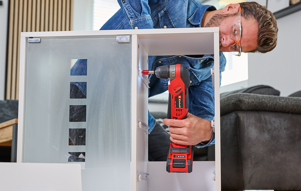 A man assembles a cabinet using an Einhell cordless angle drill.