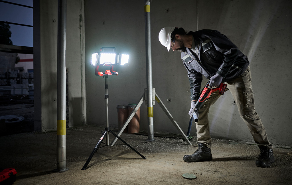 Ein Bauarbeiter nutzt eine Einhell Akku-Arbeitsleuchte auf einem Stativ, um eine dunkle Baustelle auszuleuchten.