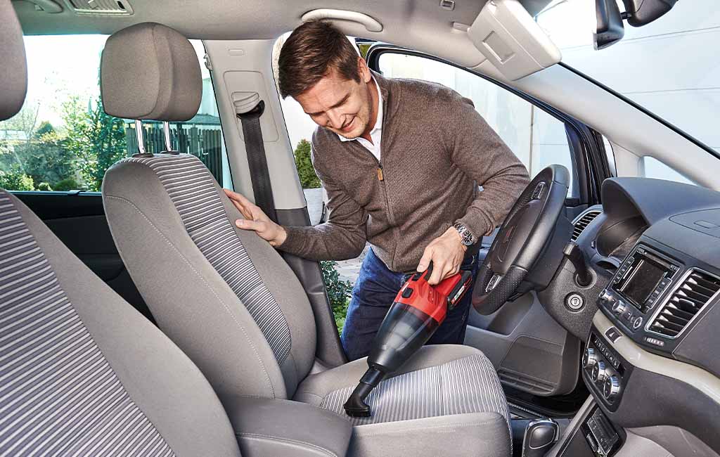 A man vacuums the driver's seat of a car with a Einhell vacuum cleaner