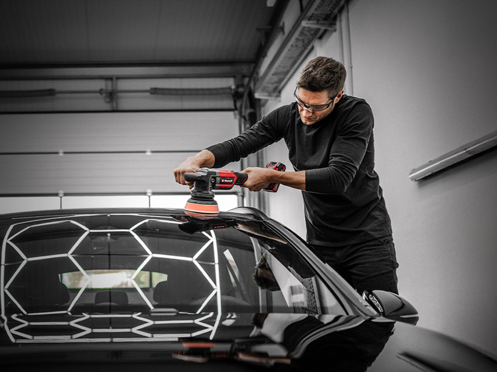 Ein Mann poliert mit einem Einhell Akku-Polierer das Dach eines Autos in einer Werkstatt.