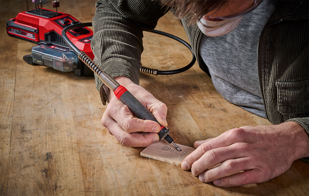 Close-up of a man engraving fine details into a small wooden plate using an engraving tool.