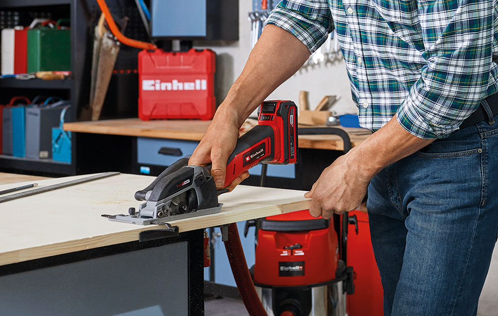 A man is cutting wood with an Einhell handheld circular saw on a workbench.