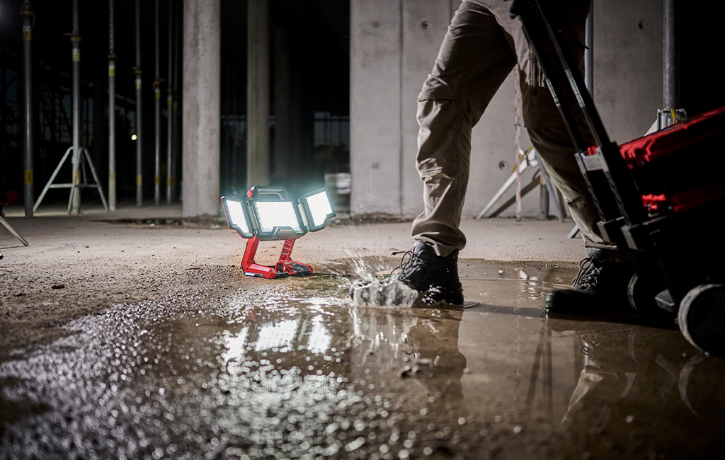 Ein tragbarer LED-Baustrahler steht auf einer Baustelle im Wasser, während eine Person vorbeigeht.