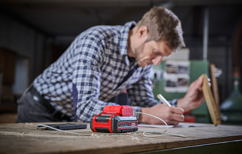 Ein Mann arbeitet an einem Tisch, während der Akku-Adapter sein Smartphone über USB auflädt.