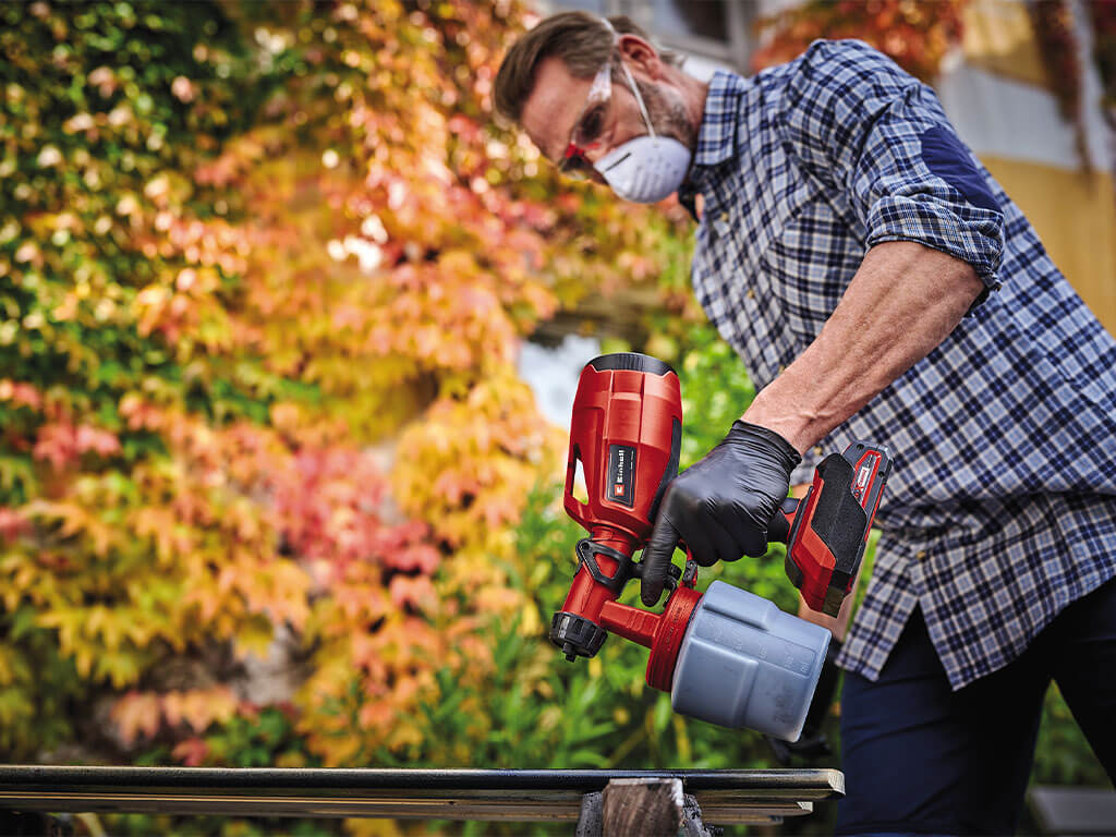 A man sprays fence slats using an Einhell paint spray system.