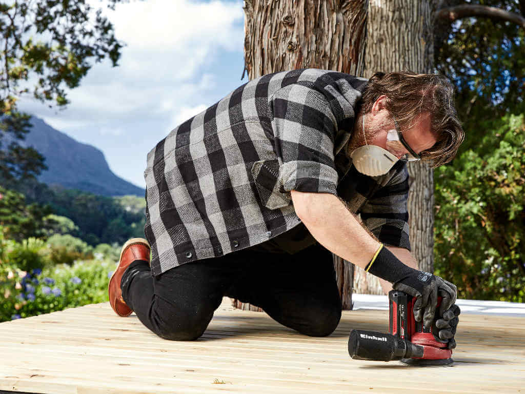 A man sands wooden boards on the floor