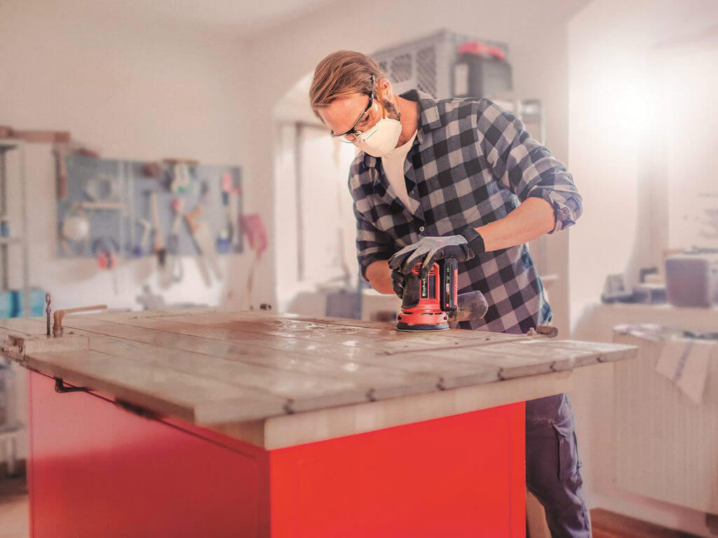 A man sands wood with a rotating sander