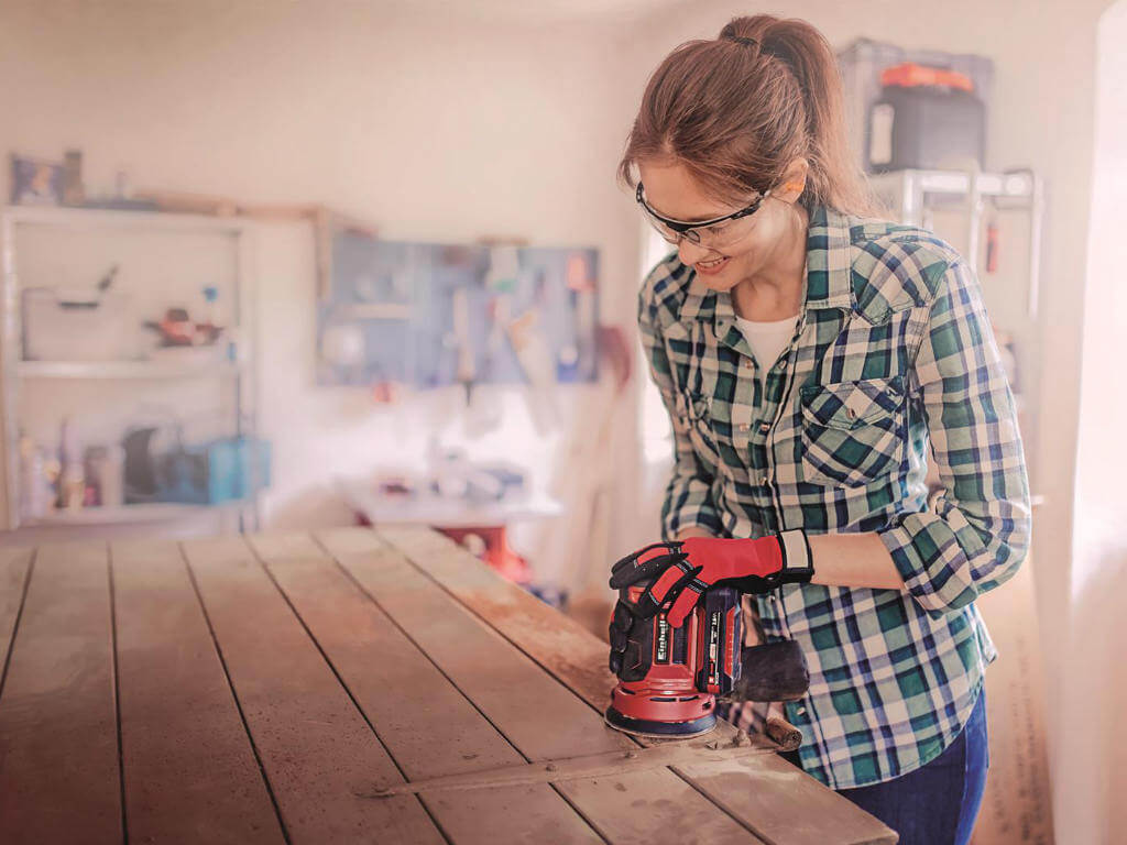 A woman sands wood with a rotating sander