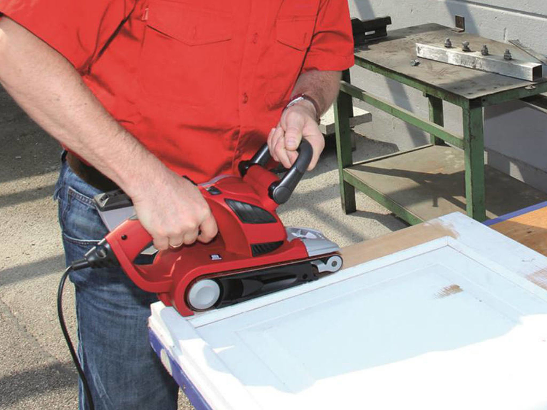 a man grinds off white paint from wood