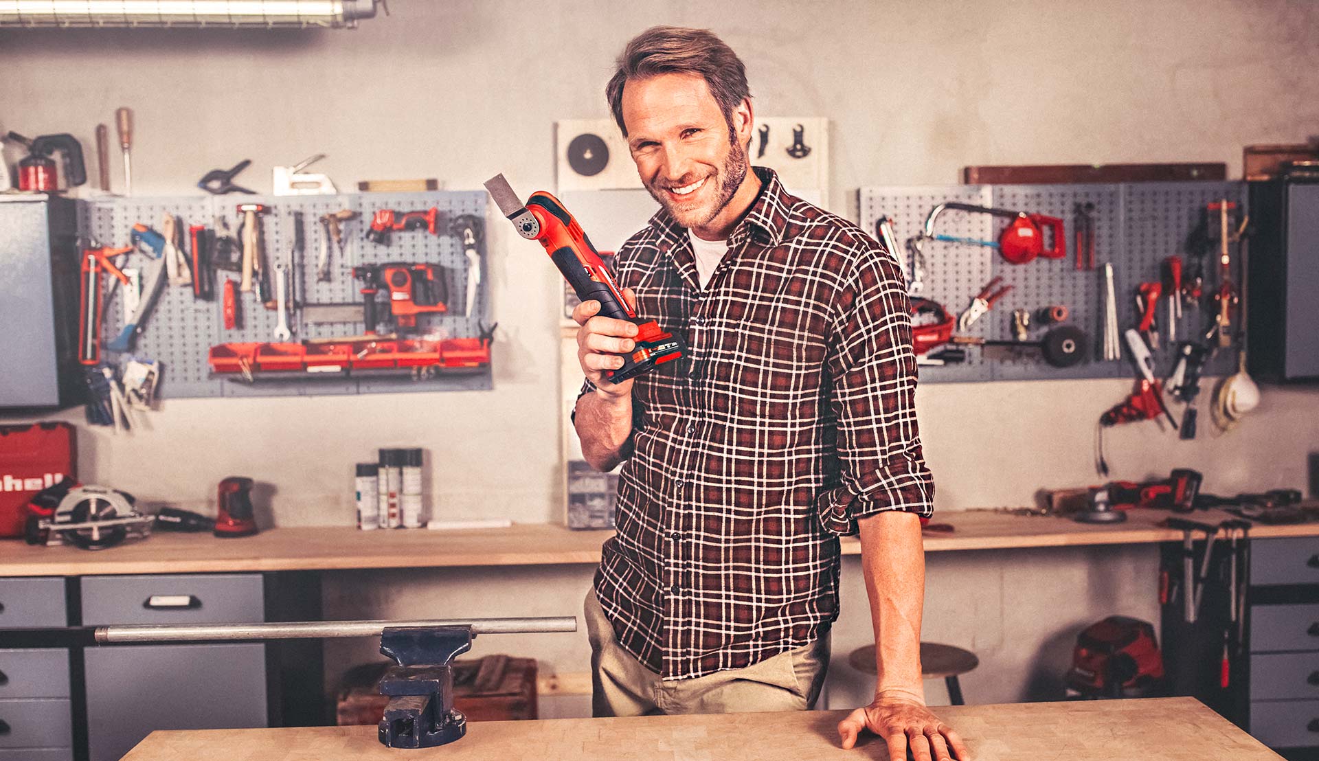 A man standing in his workshop holding a multifunctional tool in his hand.