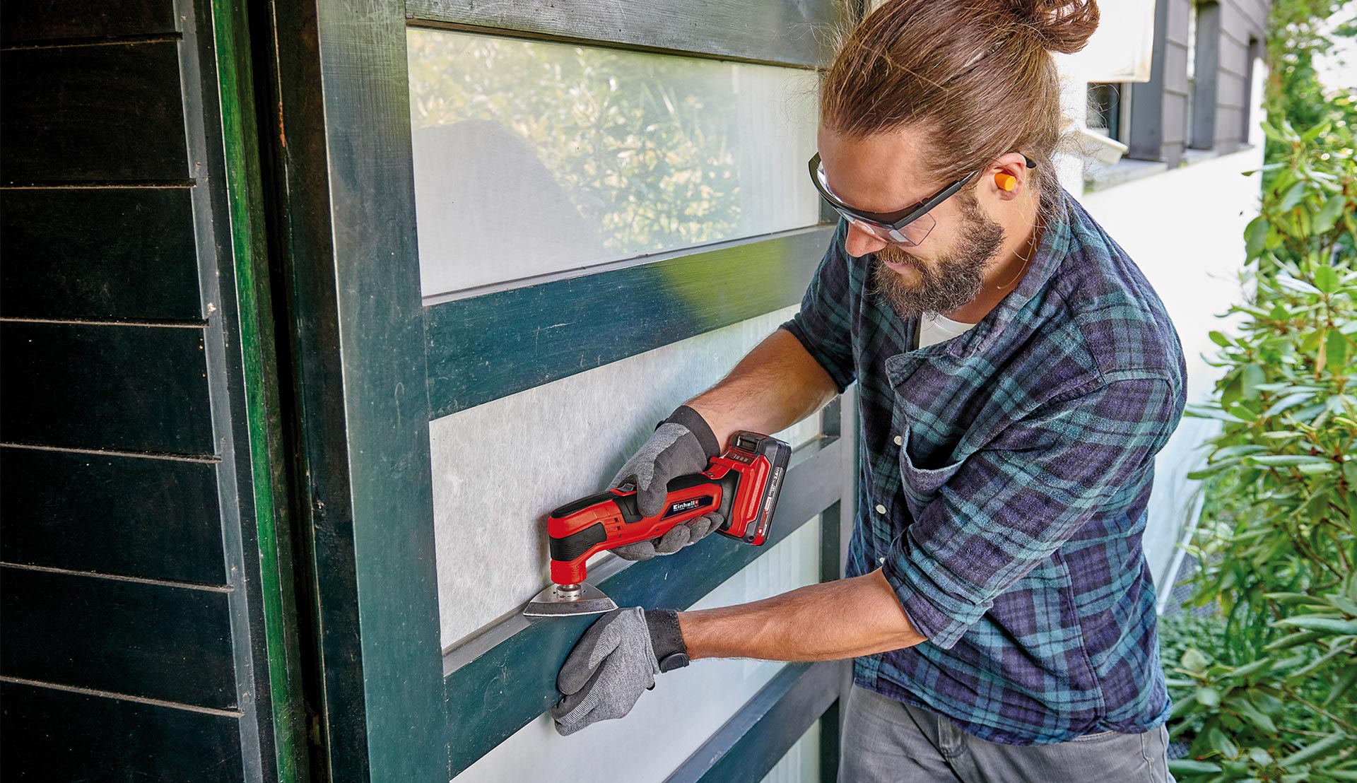 A man is using a multitool to sand a narrow wooden surface on a door.