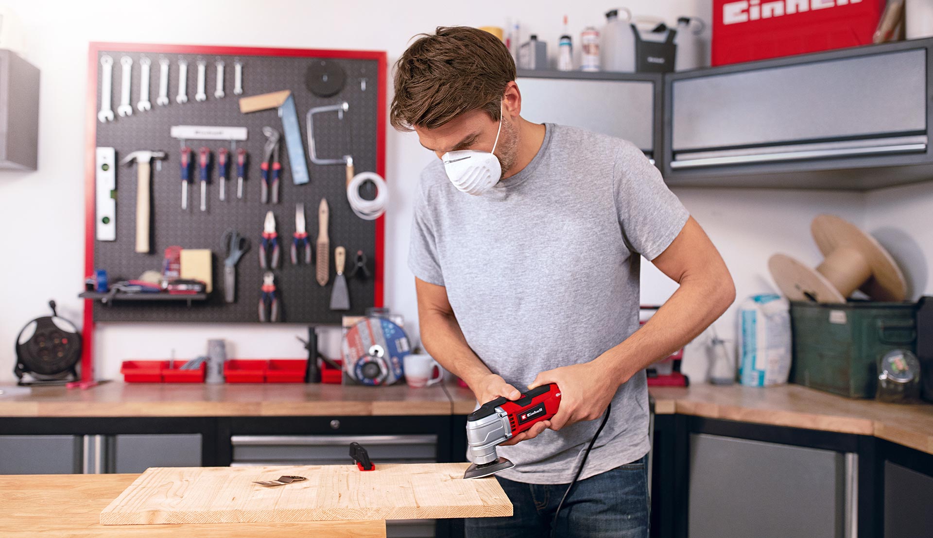 A man in a workshop working on wood using a multifunctional tool.