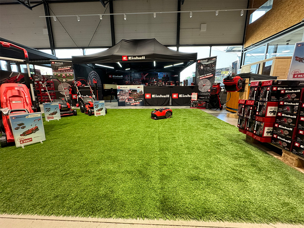 Einhell booth indoors with a focus on robotic lawn mowers and other gardening equipment displayed on artificial grass.