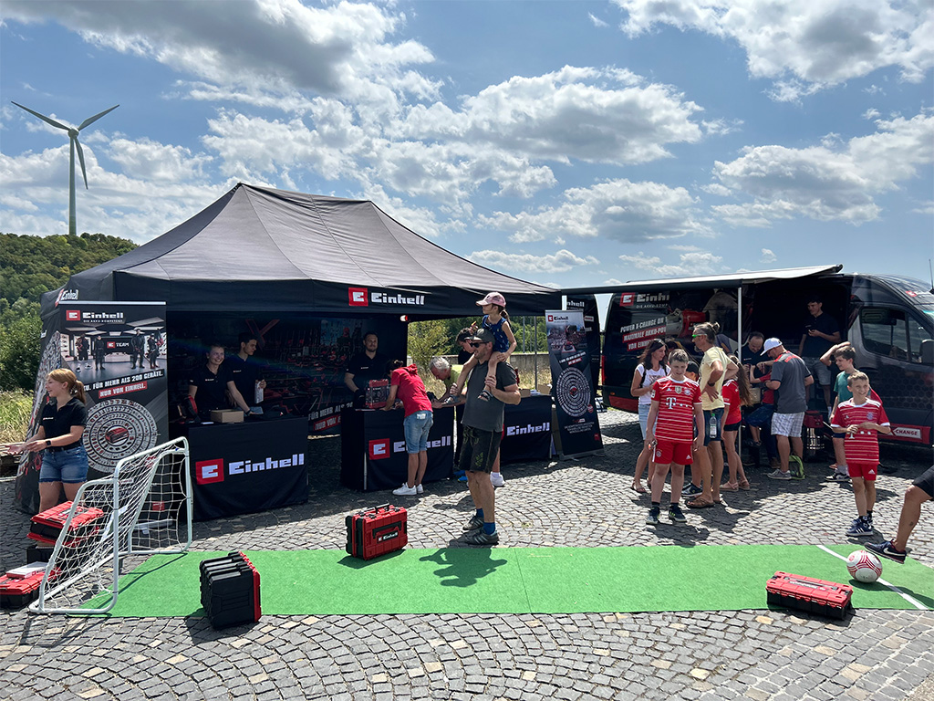 Outdoor Einhell setup featuring a tent, a van, and interactive displays with families and children engaging in activities.