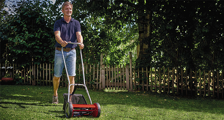 A man mowing short lawn with a hand push lawnmower.