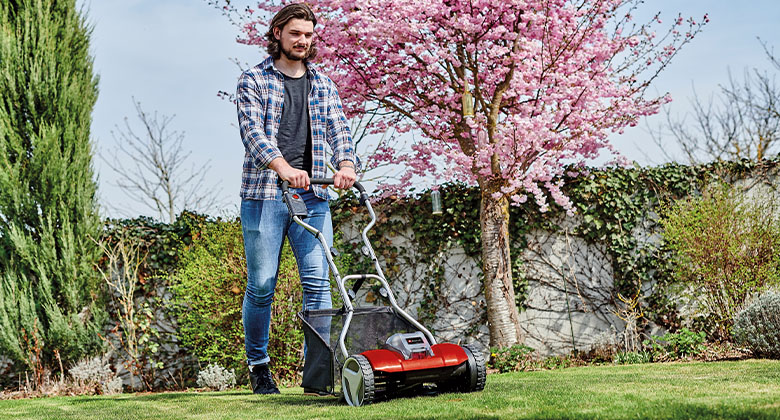 A man mowing short grass with a hand lawnmower.