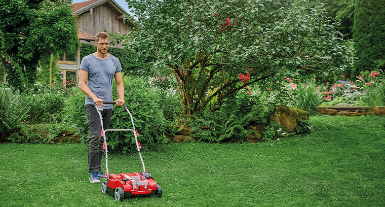 Ein Mann beim Vertikutieren des Rasens in seinem Garten mit einem Akku-Vertikutierer.