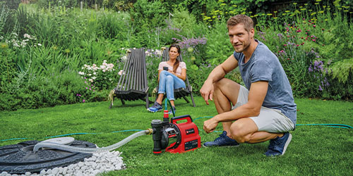 a man is sitting next to the Einhell smart pump while it is pumping water